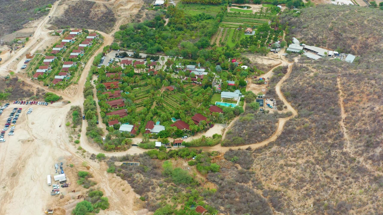 Aerial view with parking lot, cultivated fields, red roofs, and winding dirt tracks.