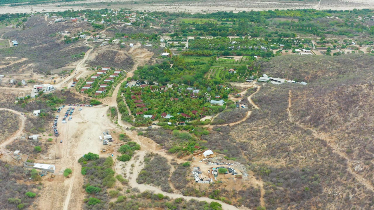 High aerial view of rural buildings, trees, dirt tracks, and scrub-covered hills.