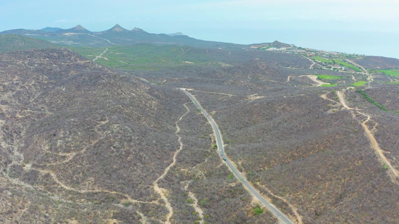 Wide drone-like view of a road descending through dry hilly terrain.