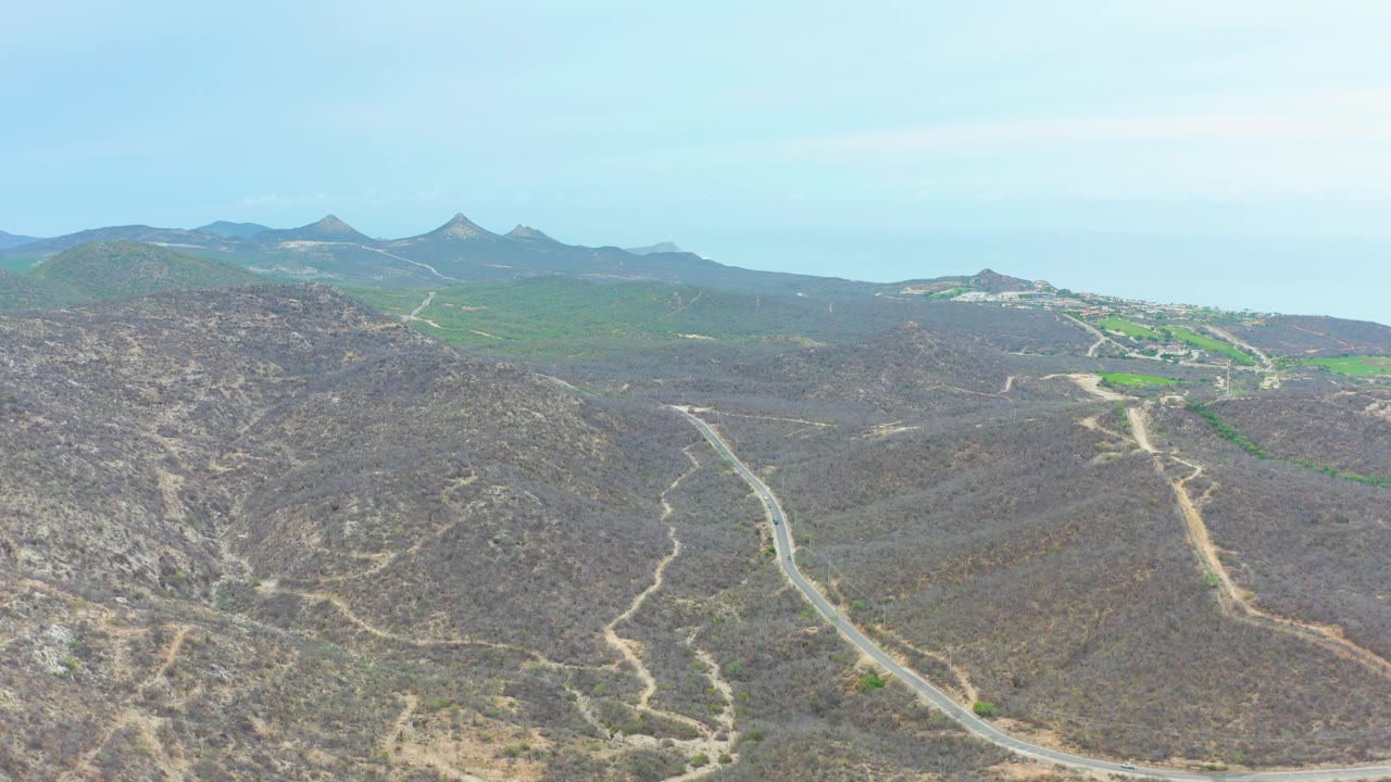 At three seconds, La Playita Los Cabos appears as dry brown hills cut by a pale winding road, with greener land and mountain peaks beyond, and no visible people.