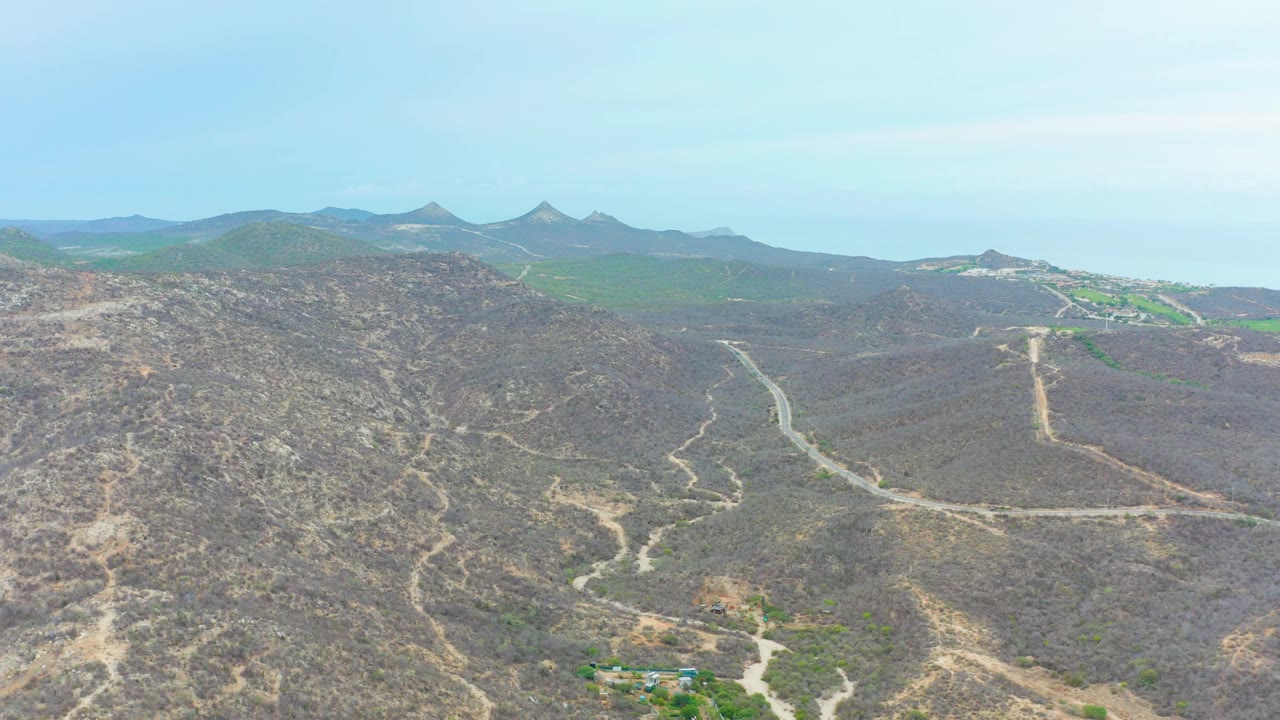 Wide aerial of arid hills with winding roads and a small settlement below.