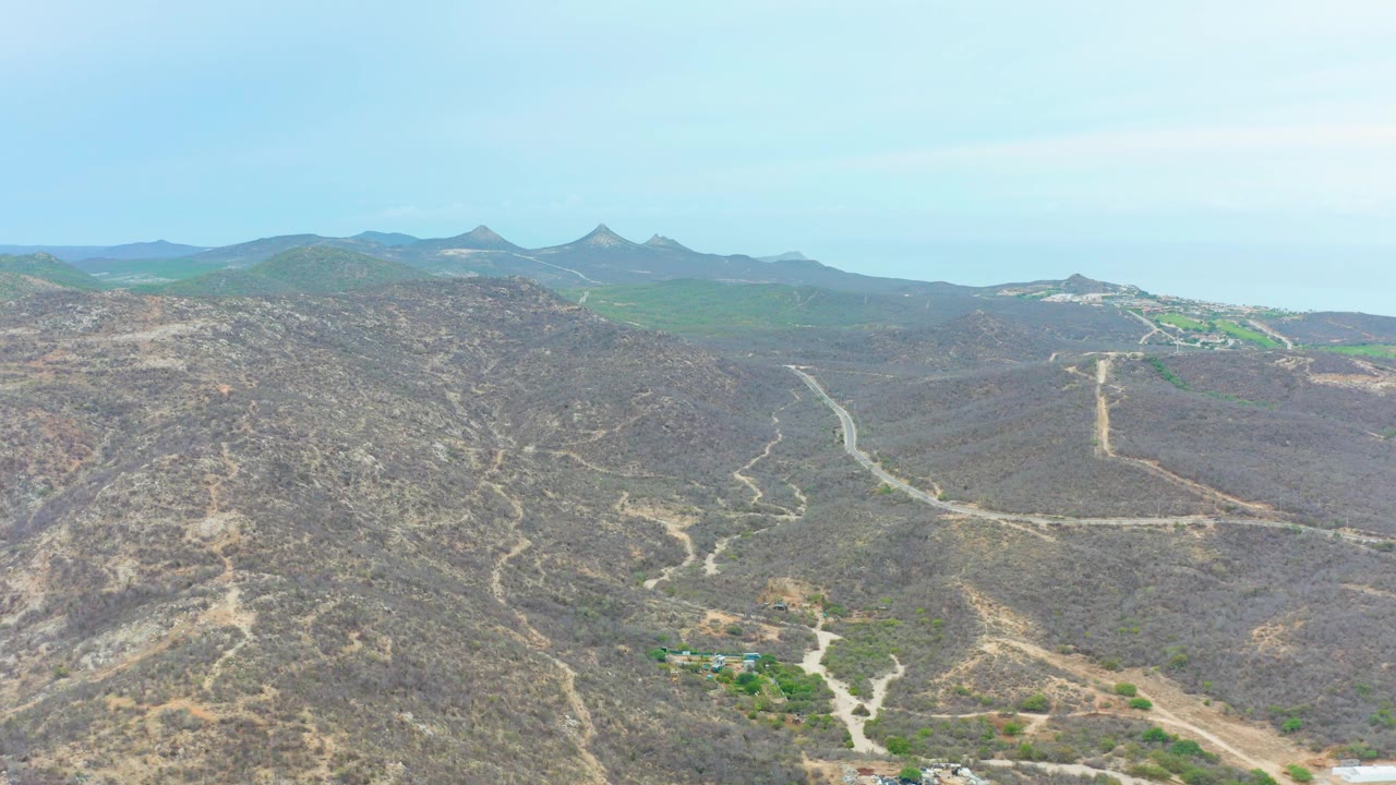 Aerial view of dry hills crossed by dirt roads under a hazy sky.
