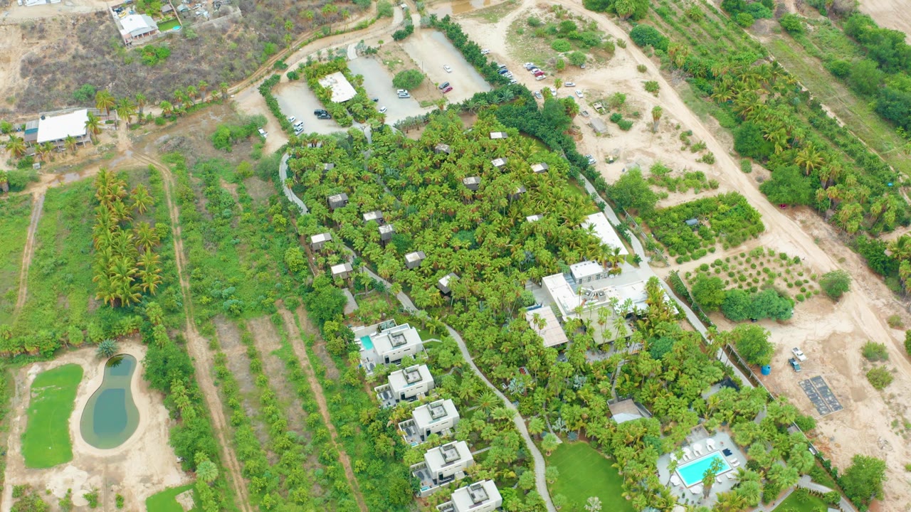 Overhead residential compound with pool, green pond, trees, cars, and pale dirt roads.