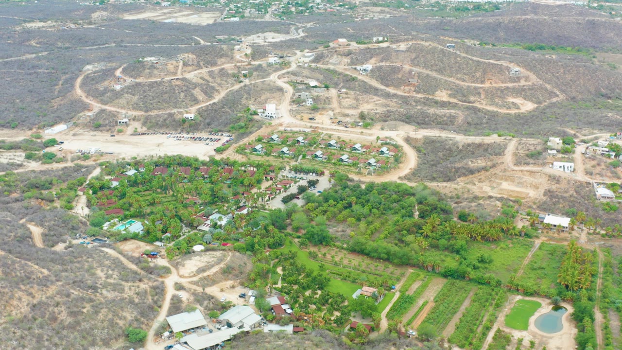 High aerial view of rural dirt roads, dry hills, green fields, trees, and buildings.