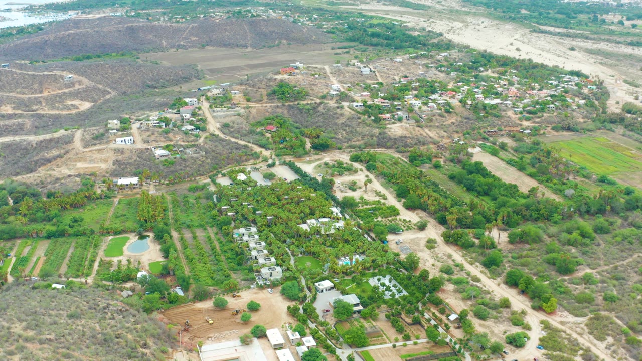 Drone view of farmland rows, small buildings, dirt tracks, and arid hills.