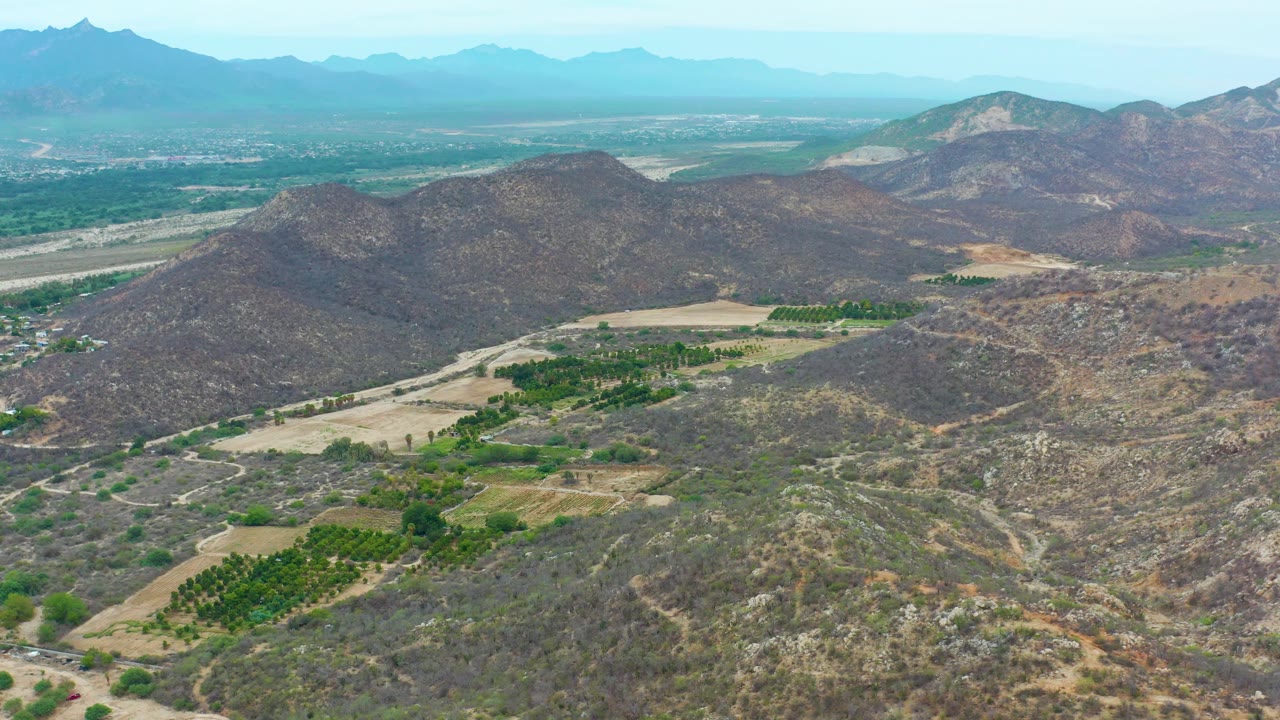 Aerial view of dry hills, green fields, and distant mountains.