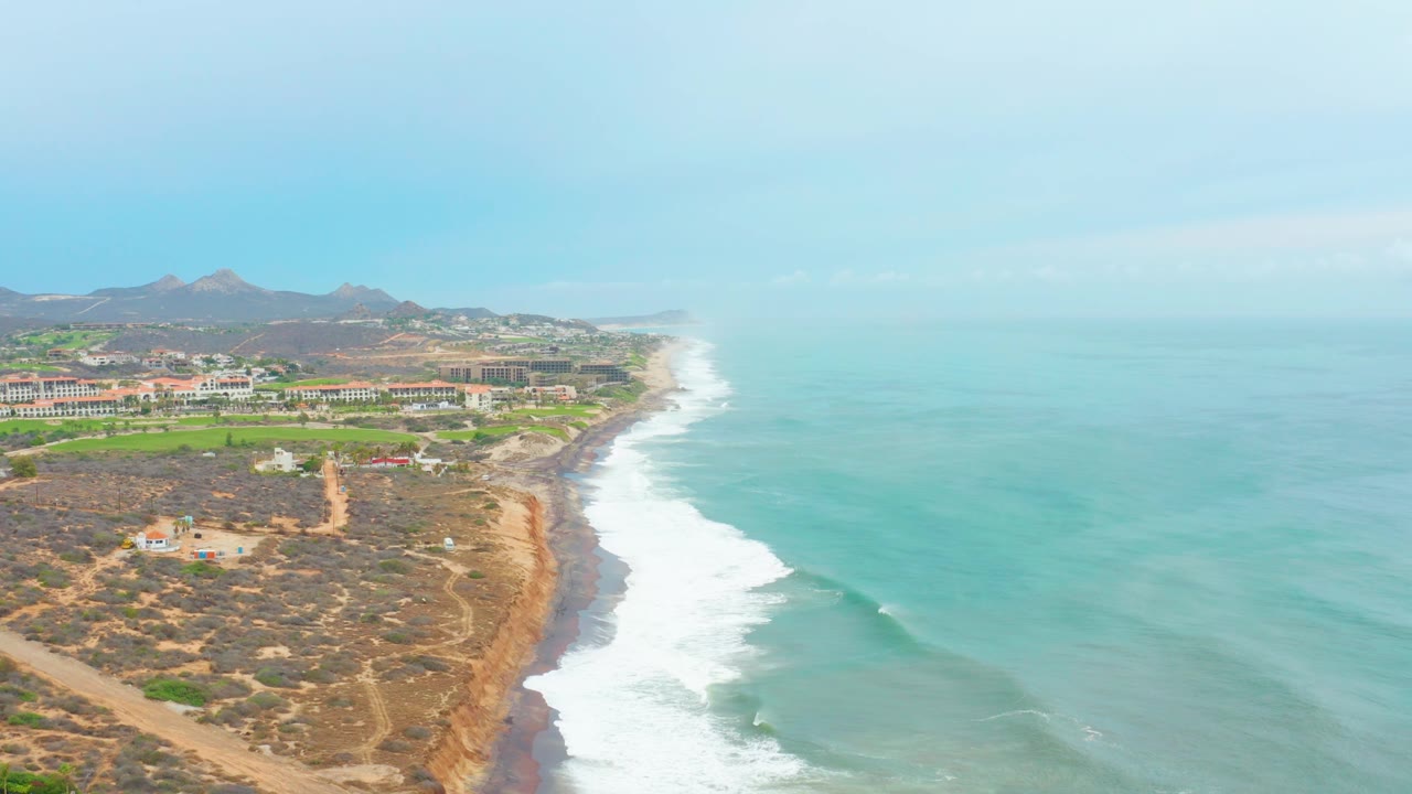Aerial coastline view with a long surf line and dry road network on the hillside.