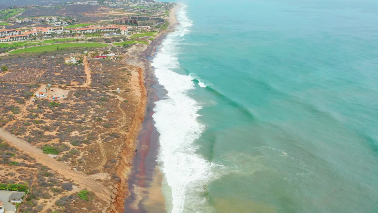 Coastal dunes and foamy surf viewed from above with ocean filling the right side.