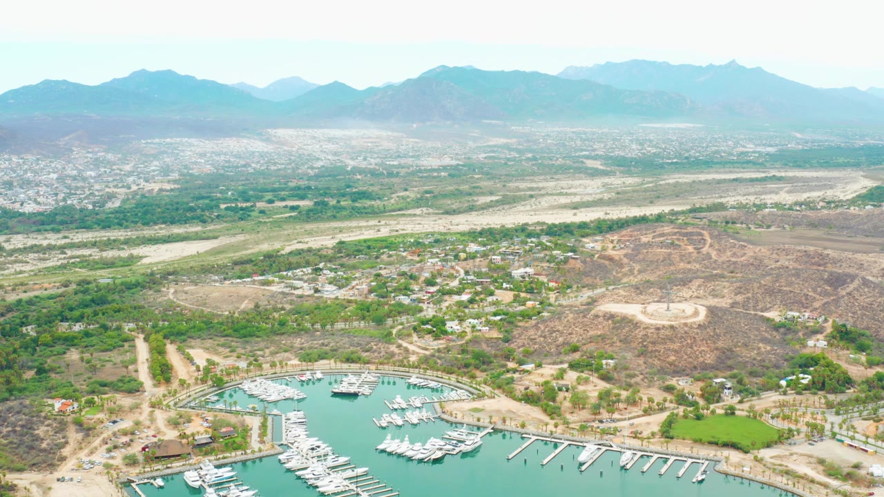 Wide drone view of marina below dry hills and a distant city.