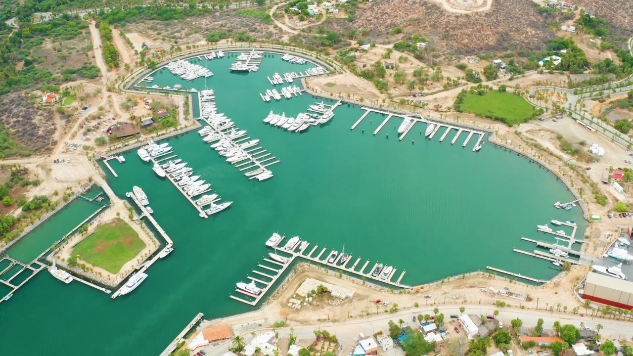 High-angle marina view with rows of boats, docks, green water, and hillside roads.