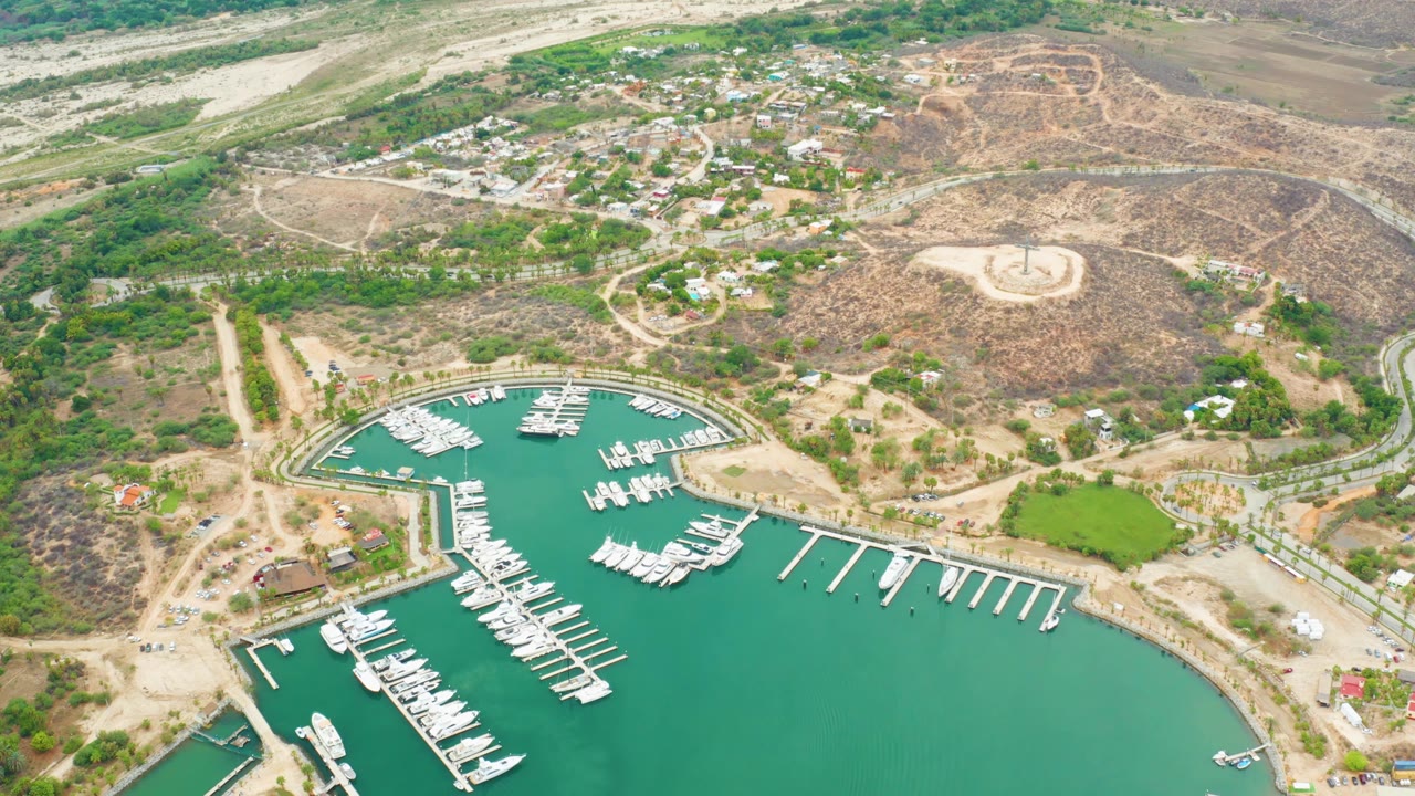Aerial marina basin with boats, finger docks, road, settlement, and arid hillside.