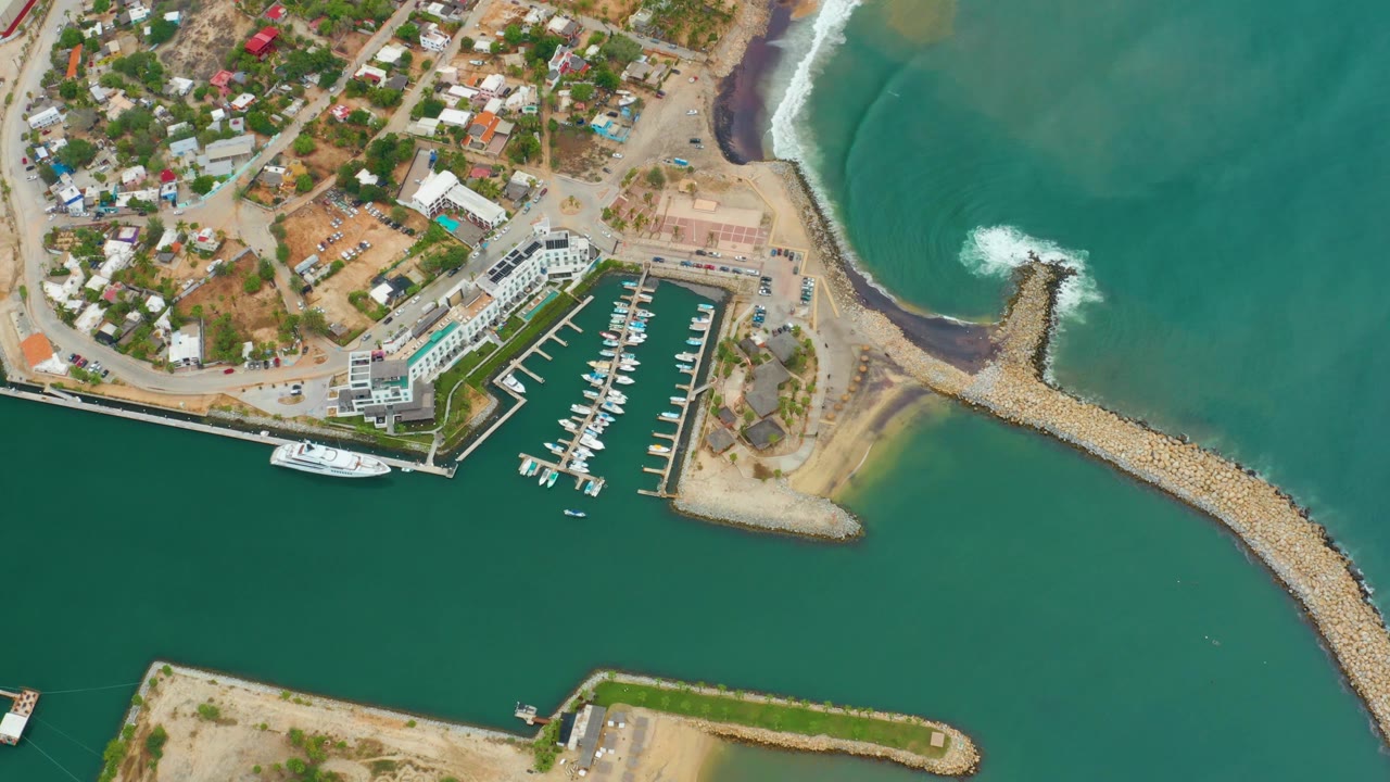 Overhead marina with docked boats and surf hitting the breakwater.