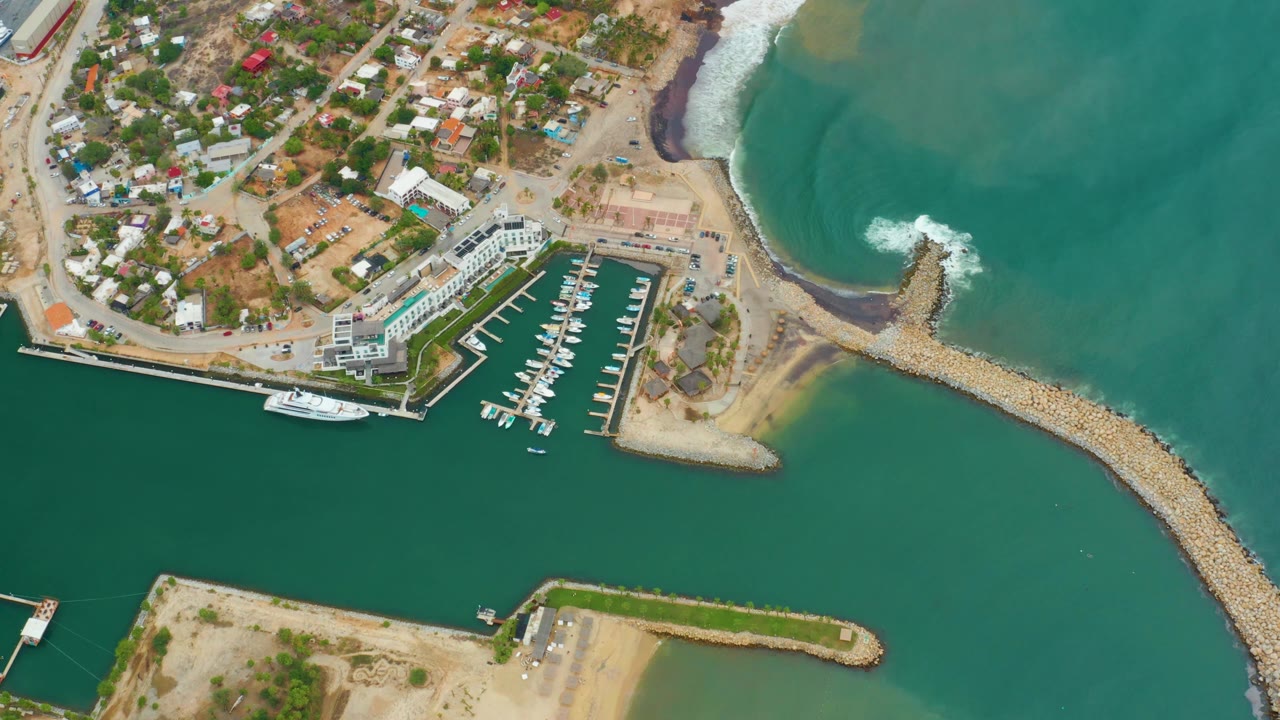 Overhead view of breakwater, surf foam, docks, and coastal settlement.