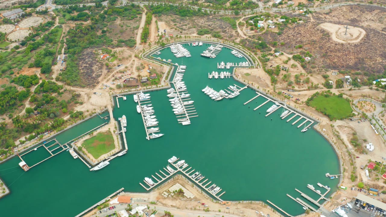 Aerial marina with teal water, docks, boats, roads, and dry hills.