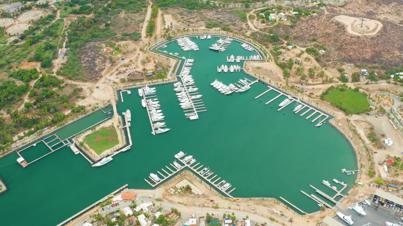 Aerial harbor frame with moored boats, marina docks, green water, and dry terrain.