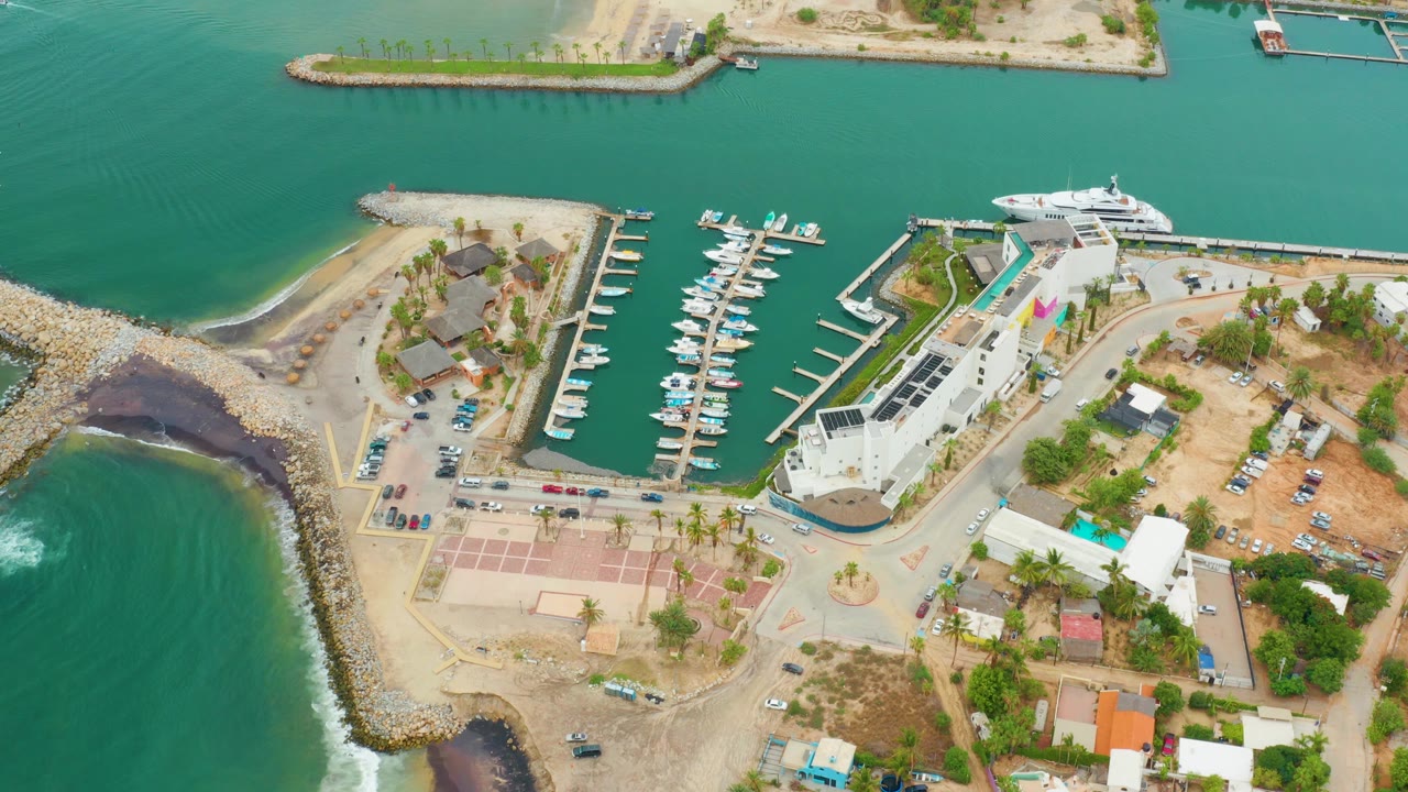High overhead marina view with boats in slips and surf against the breakwater.