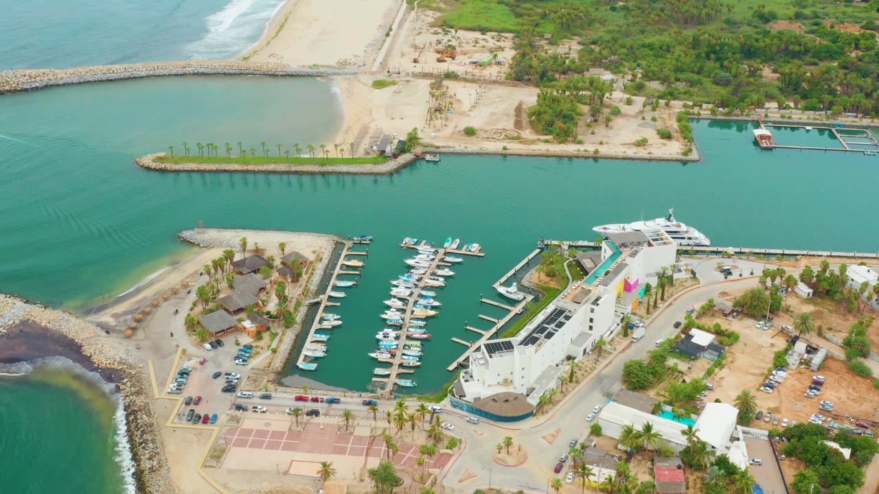 Aerial marina view with boats, breakwater, beach, road, and parking lot.