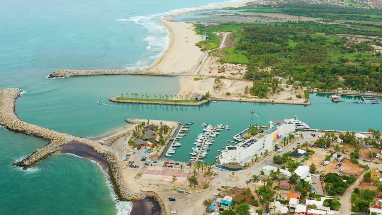 High aerial view of harbor entrance, docked boats, sandy beach, and greenery.