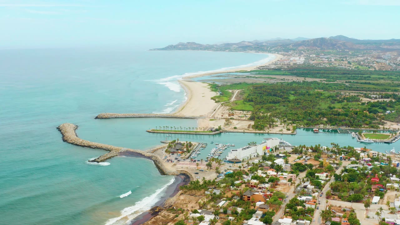 Drone view of shoreline, marina basin, breakwaters, and coastal buildings.