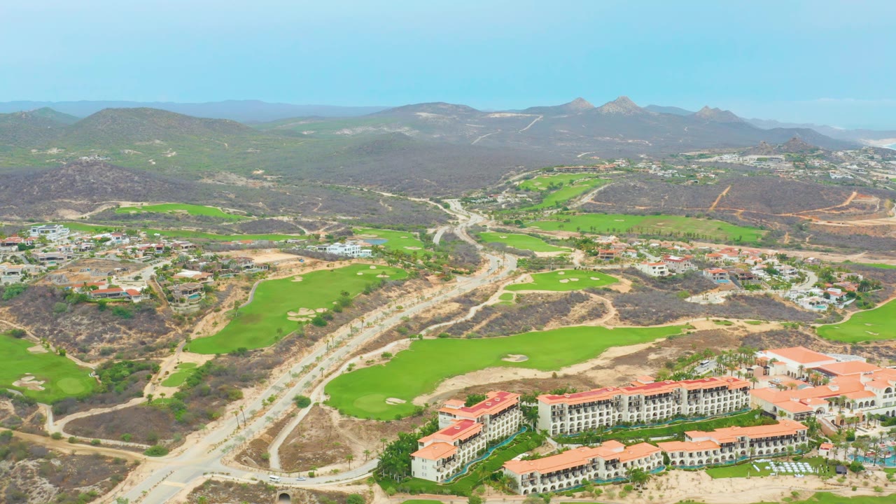 Aerial view of golf course, resort buildings, road construction, and mountains.
