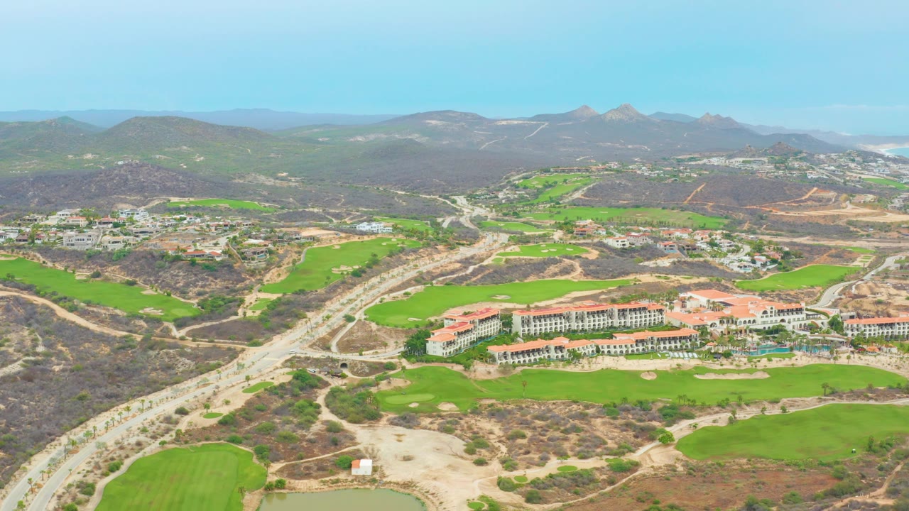 Aerial landscape with golf fairways, highway, buildings, and hazy mountains.