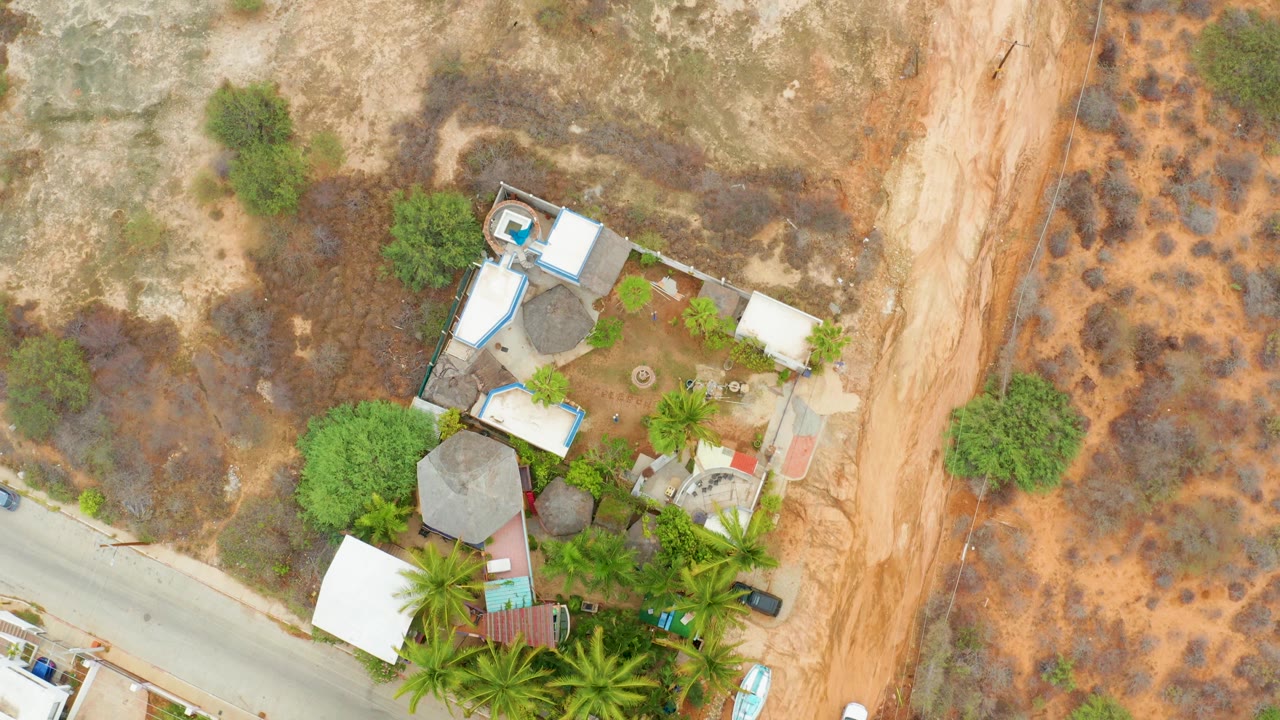 Top-down aerial view of a roadside compound, trees, dry terrain, and a diagonal road.