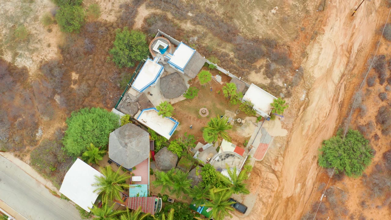Aerial view of a residential compound, road, trees, and brown dirt terrain.