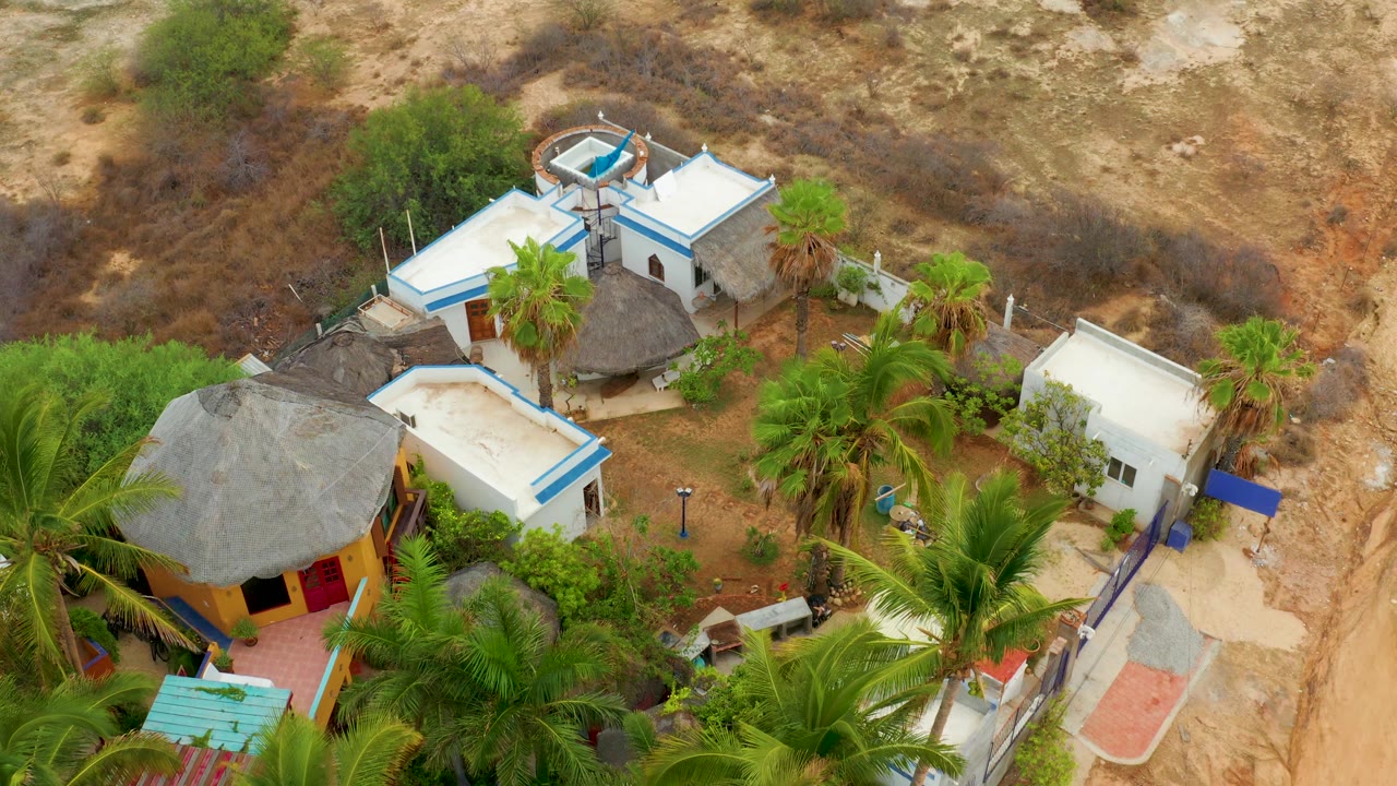 High view of a yellow building with a thatched roof beside white buildings and palms.