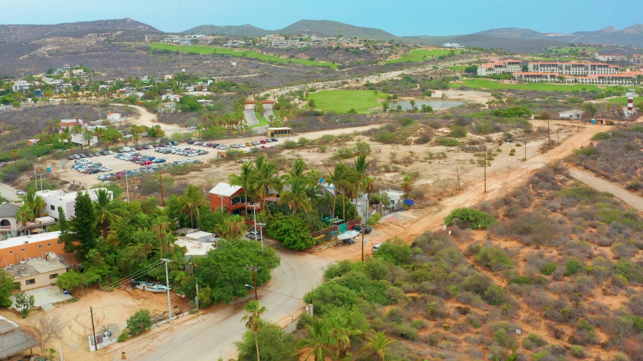 Aerial view with parking lot, palms, dirt roads, dry hills, and green fields.
