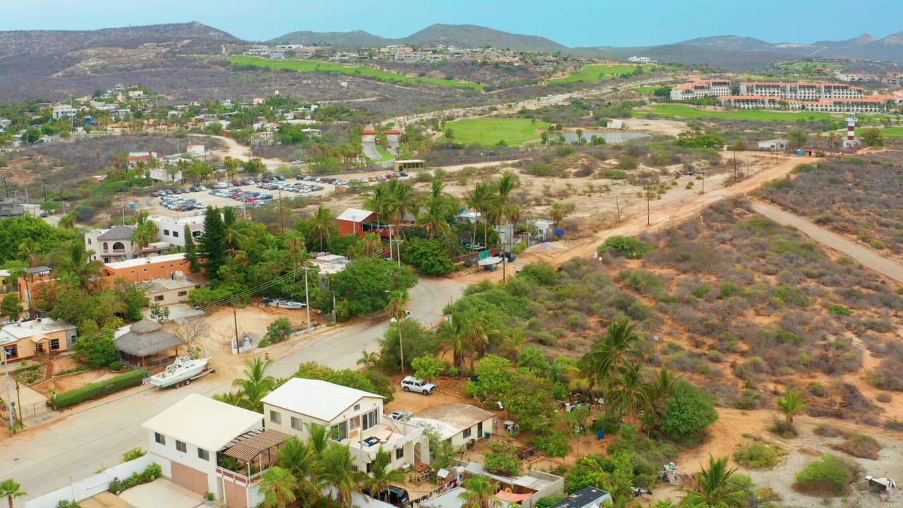 Residential edge with road, palms, dry hillside, and green fields.