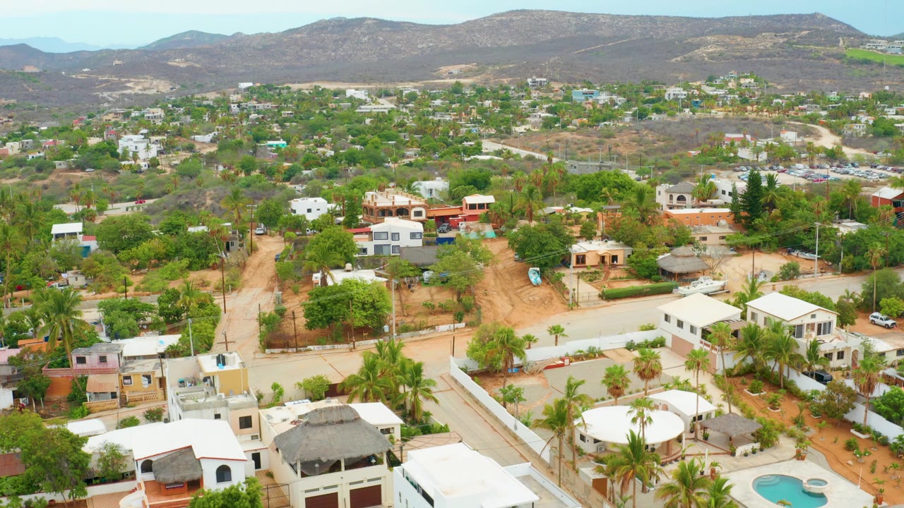 Aerial neighborhood view with dirt road, houses, palms, and dry mountains.