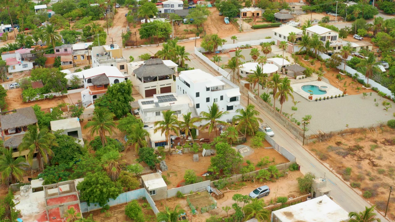 Drone view of a residential road beside walled homes and palms.