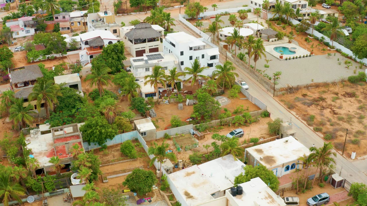 Aerial view of homes, palms, a central street, and sandy residential lots.