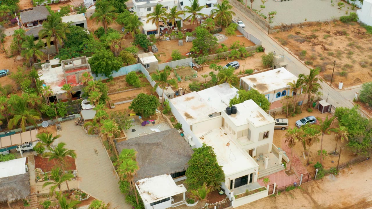 Drone view of homes, palm trees, sandy lots, road edges, and parked cars.