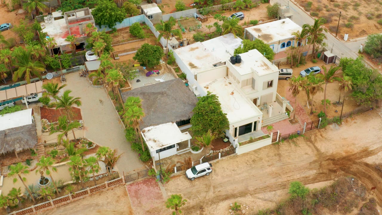 Aerial neighborhood view with a dirt road, palm trees, white homes, and dry ground.