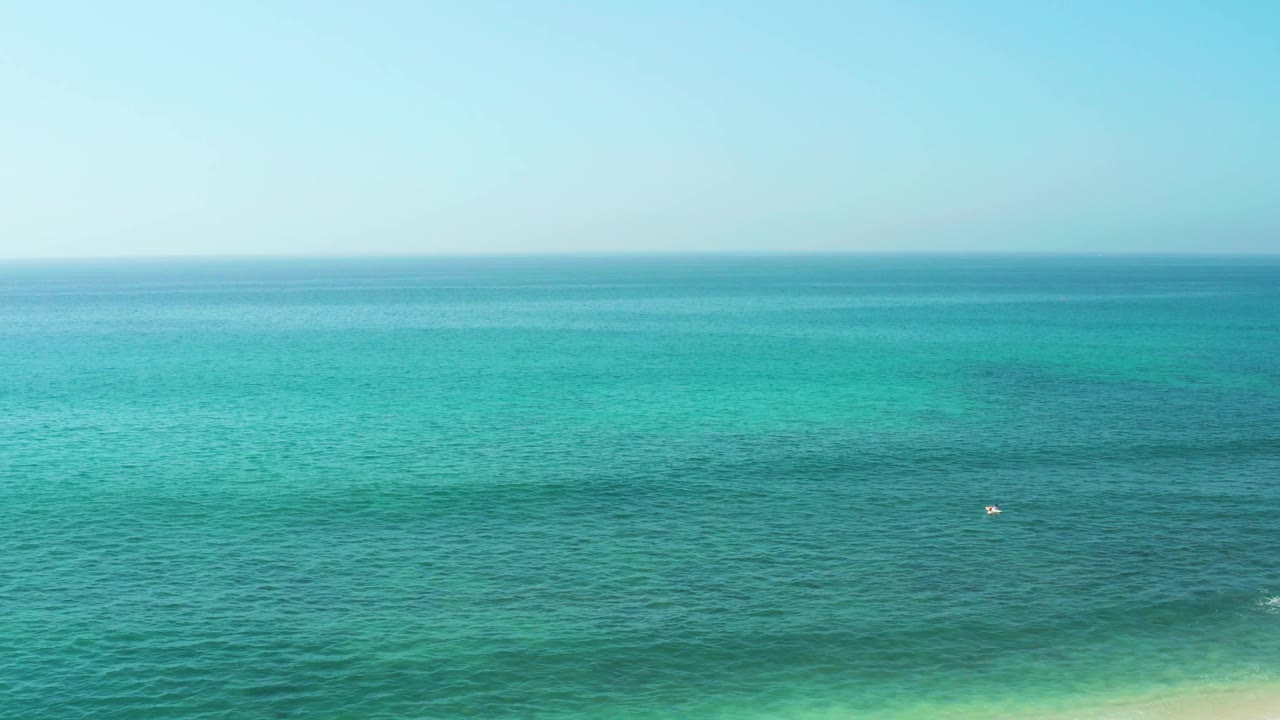 Open turquoise water with a small distant swimmer or object near the center.