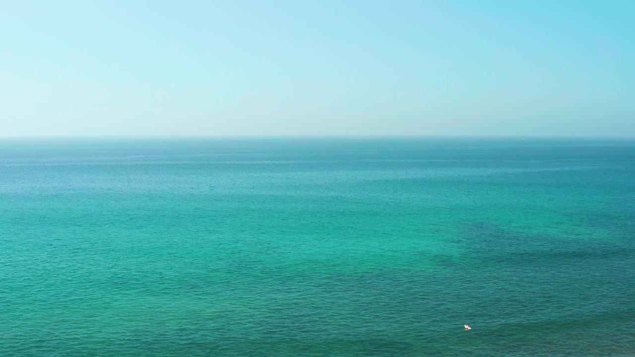 Turquoise ocean with pale sky and a small white buoy near the lower center.