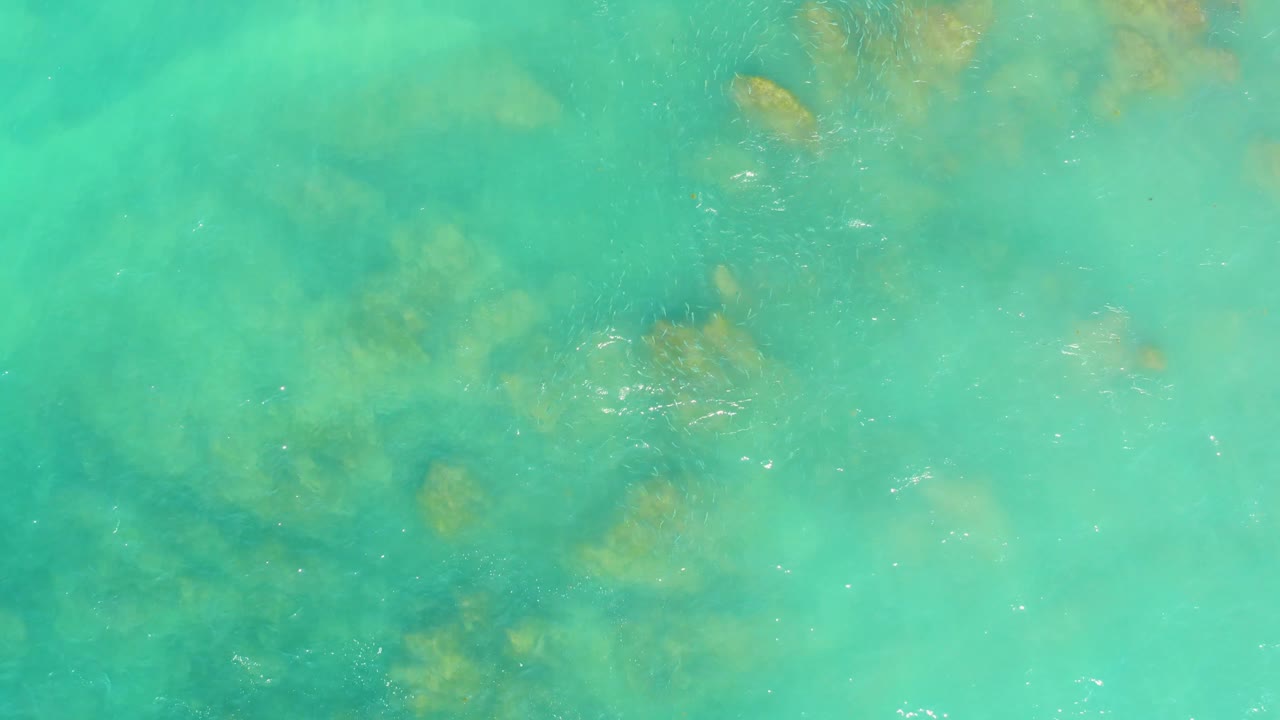 Pale turquoise water at El Tule Beach Los Cabos appears slightly softer in tone, with diffuse seaweed or coral patches below and no visible people.