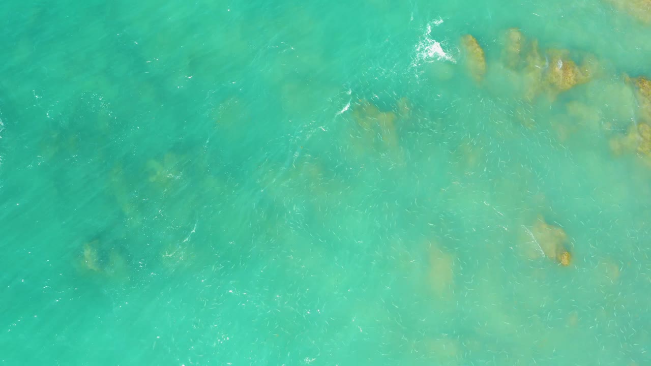 Turquoise-green ocean water at El Tule Beach Los Cabos shows scattered submerged rock patches and light ripples, with no visible people.