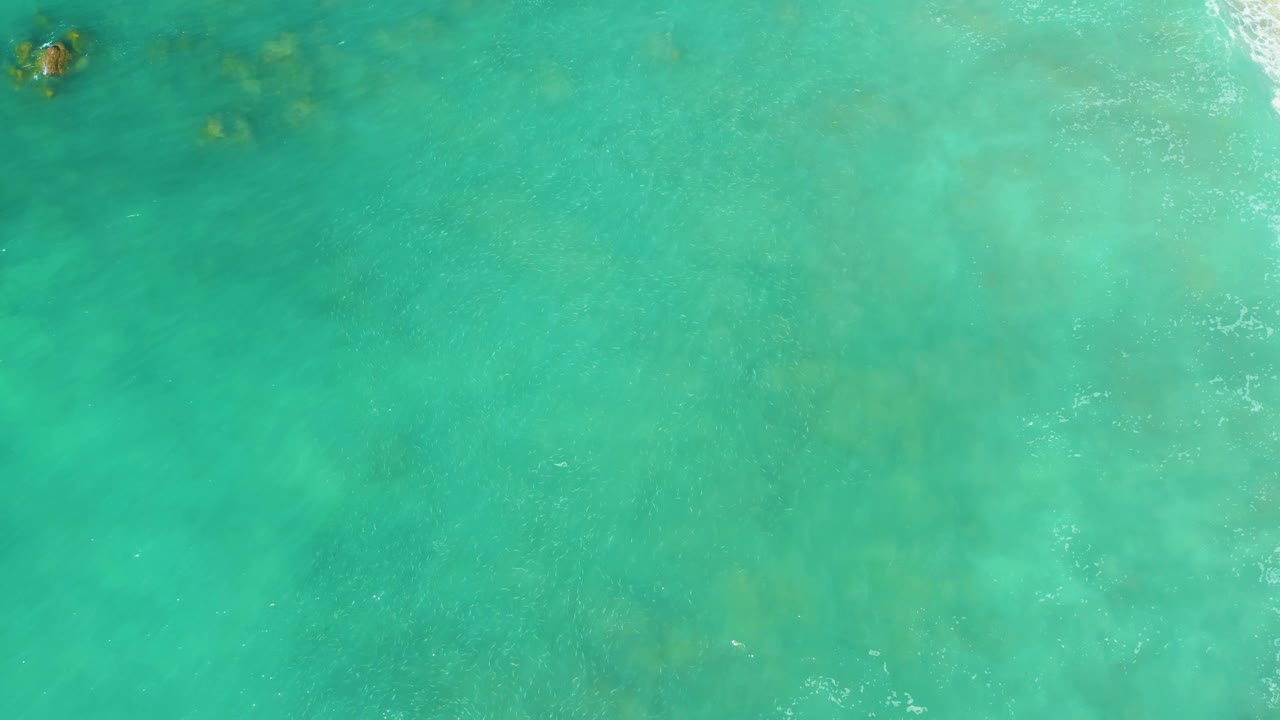 Clear turquoise ocean with a small swimmer near the top edge.
