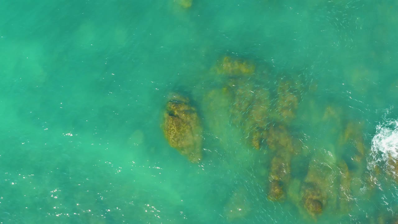 Clear turquoise water over underwater rocks with ripples and foam near the right edge.