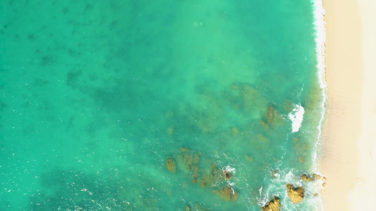 Aerial view of shallow turquoise water washing over rocks by sand.