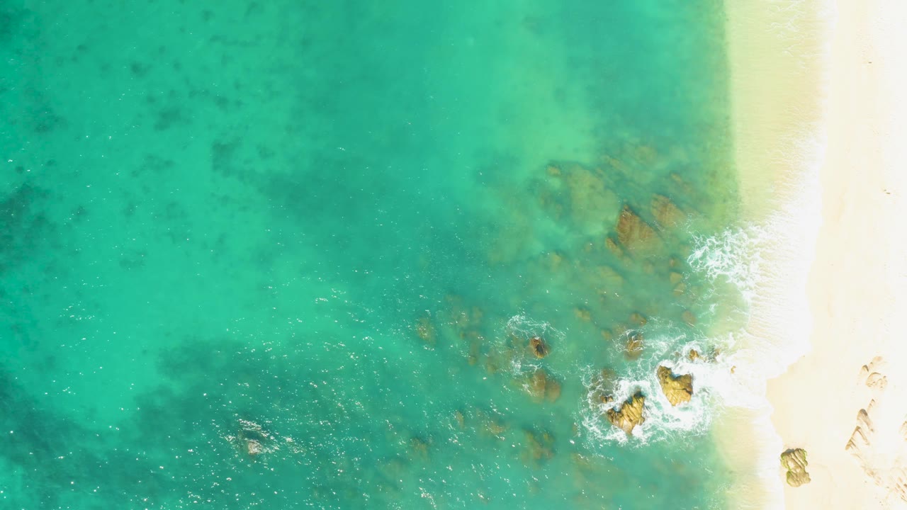 Clear shallow water and sandy shoreline with rocks under small waves.