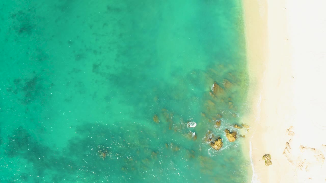 Clear shallow water and sandy shore with small foam near rocks.