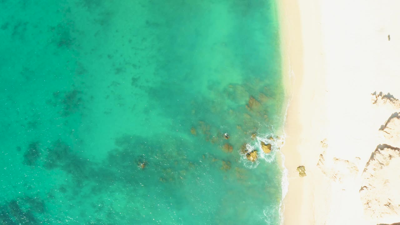 Top-down view of turquoise water meeting pale sand