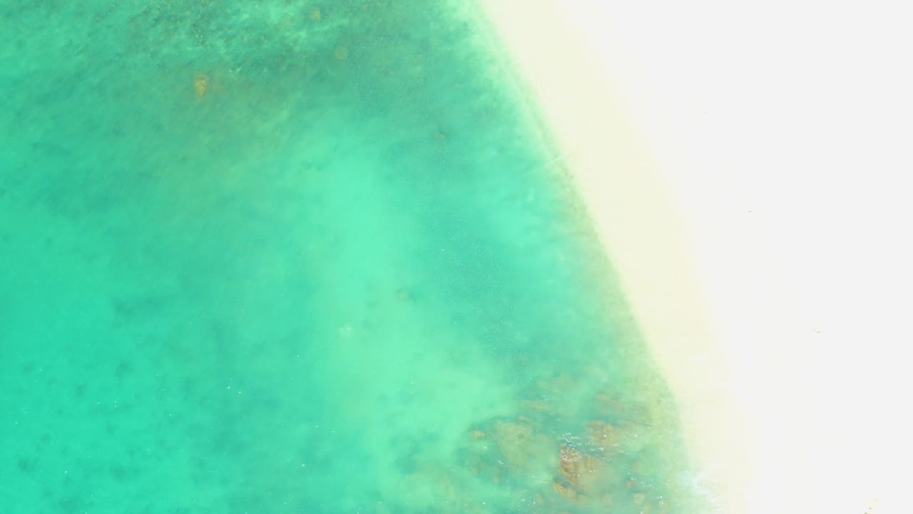 Turquoise shallow water beside a bright sandy shoreline.