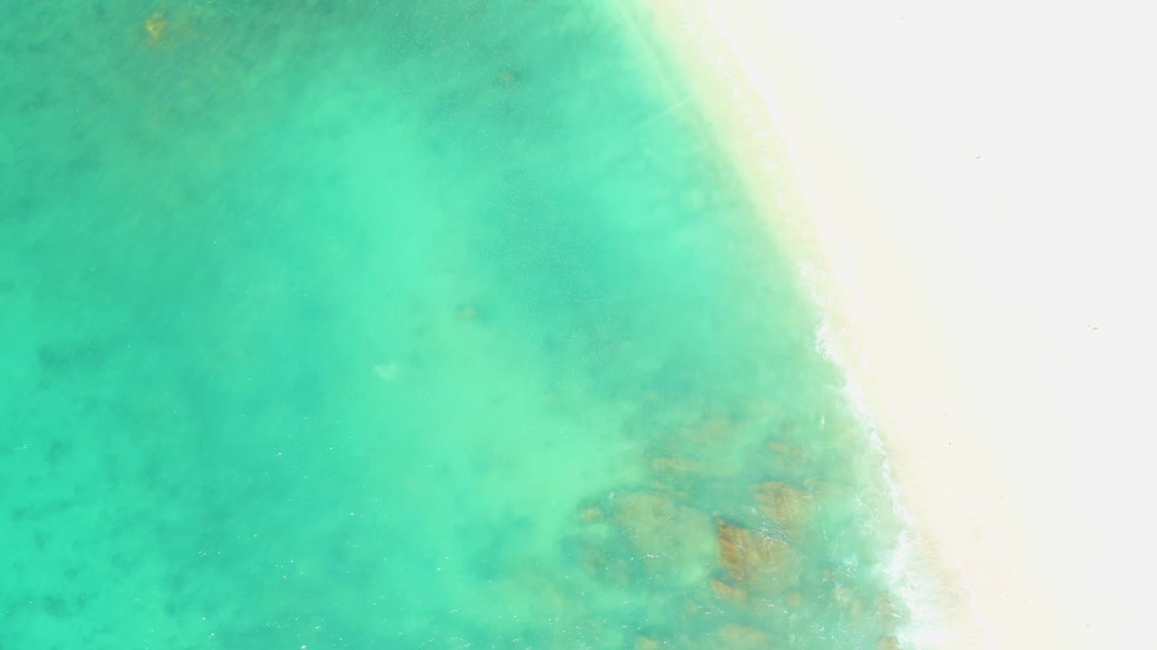 Turquoise shallows at El Tule Beach press closer to the white sand edge, with the waterline softened by light wave movement and no visible people.