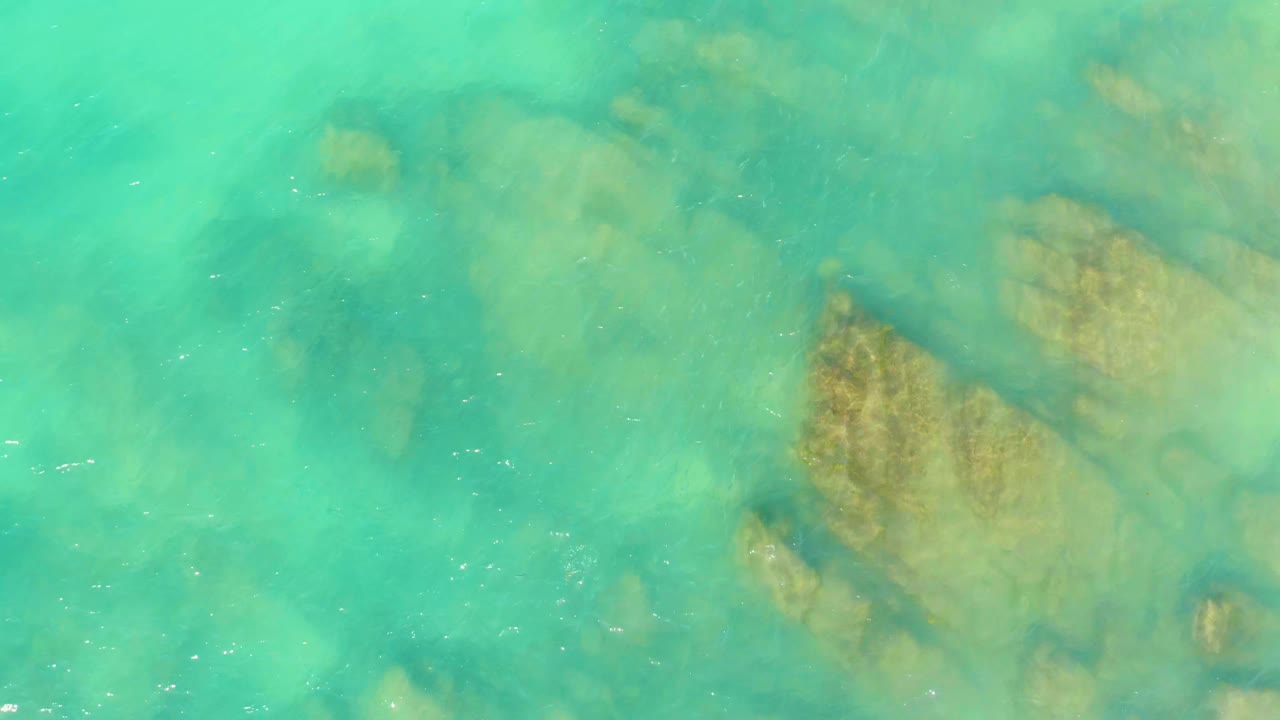 At one second, the overhead view shows green-blue transparent water with a larger brown rock formation right of center and no visible people.