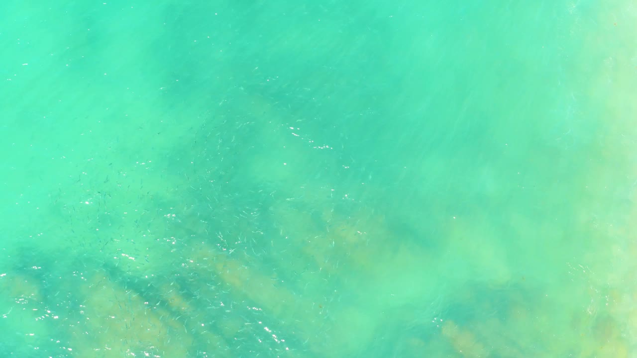 A turquoise ocean surface at El Tule Beach in Los Cabos carries pale reflected light over muted submerged rocks, with no visible people.