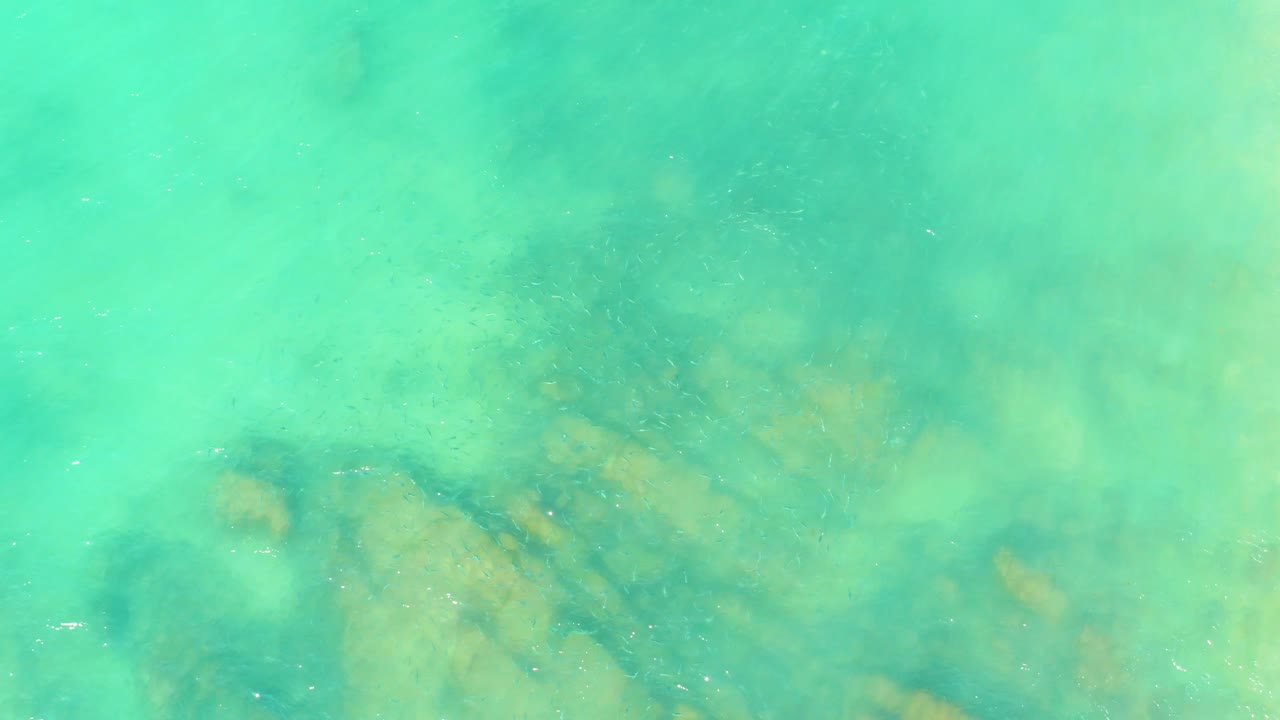 A top-down frame of green-blue ocean water at El Tule Beach in Los Cabos shows hazier rock shapes below the surface and no visible people.